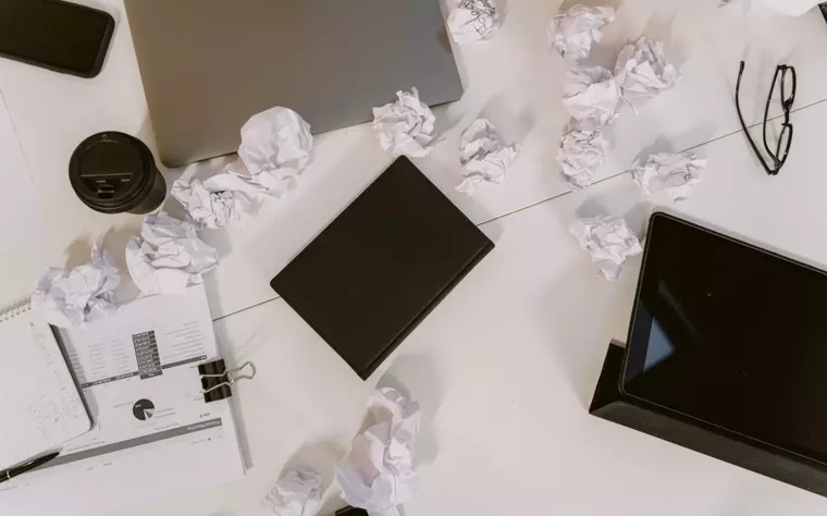 Escritorio cubierto de papeles arrugados y hojas sueltas junto a una laptop