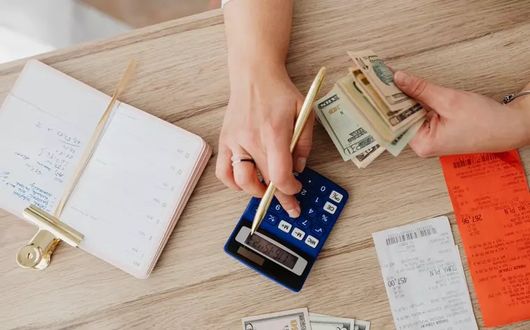 Manos usando una calculadora entre recibos y billetes sobre un escritorio