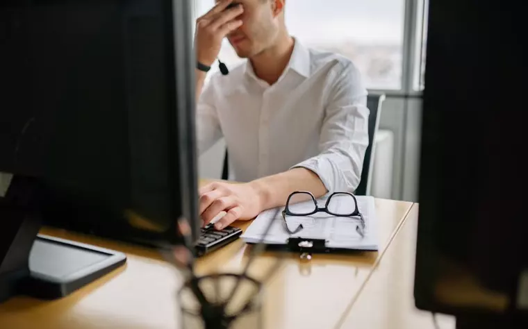 Persona con la cabeza entre las manos frente al monitor de la oficina